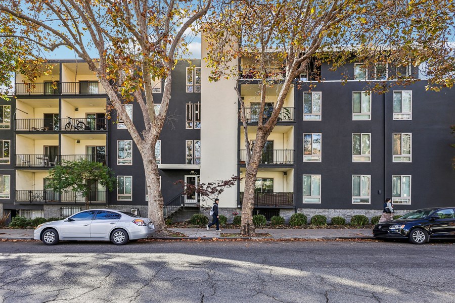 A white car is parked on the street in front of a gray building.
